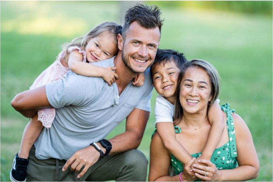 A smiling family of four together outdoors.
