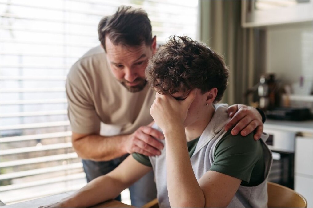 A caregiver leaning in to comfort a teenager during a hard moment at home.